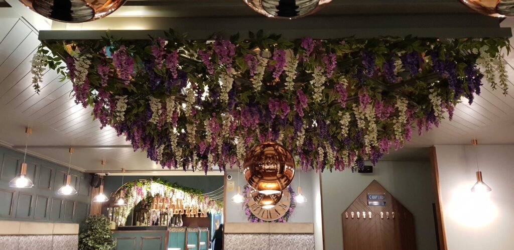 A stunning display of purple, pink, and white artificial wisteria on the ceiling of the Grape & Grain wine bar